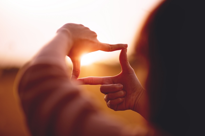 A person holding up a square shape with the sun in the background, symbolizing our vision of making a positive impact in our community.
